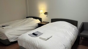 A hotel room with two single beds, a nightstand with a lamp, and a chair. - Fuji Premium Hotel (Fujiyoshida)
