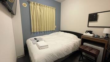 A hotel room with a bed, a desk, a chair, a lamp, and a window with curtains.