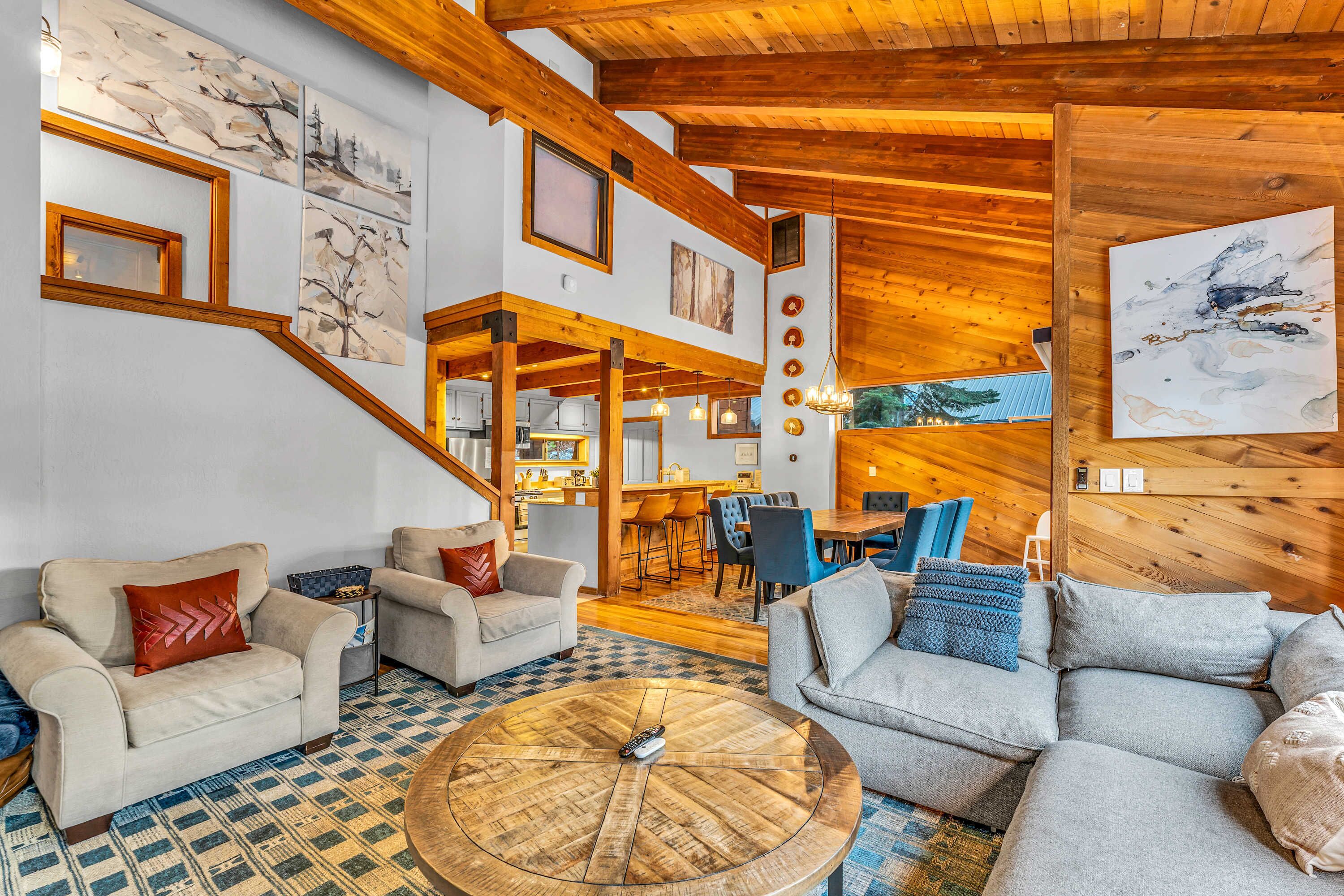 A spacious living area with a large wooden ceiling, a dining area, and a staircase leading to an upper level.