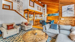 Un amplio salón con un gran techo de madera, un comedor y una escalera que lleva a un nivel superior.