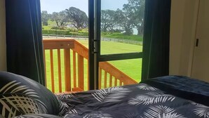 Une chambre avec un lit, une vue sur une pelouse verdoyante et une terrasse en bois à l’extérieur de la fenêtre.
