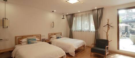 A hotel room with two beds, a chair, a hanging light fixture, and a view of the outside.