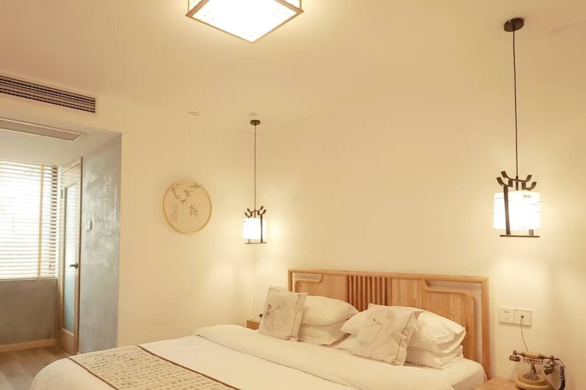 A bedroom with a bed, bedside tables, a wall clock, and ceiling lights.