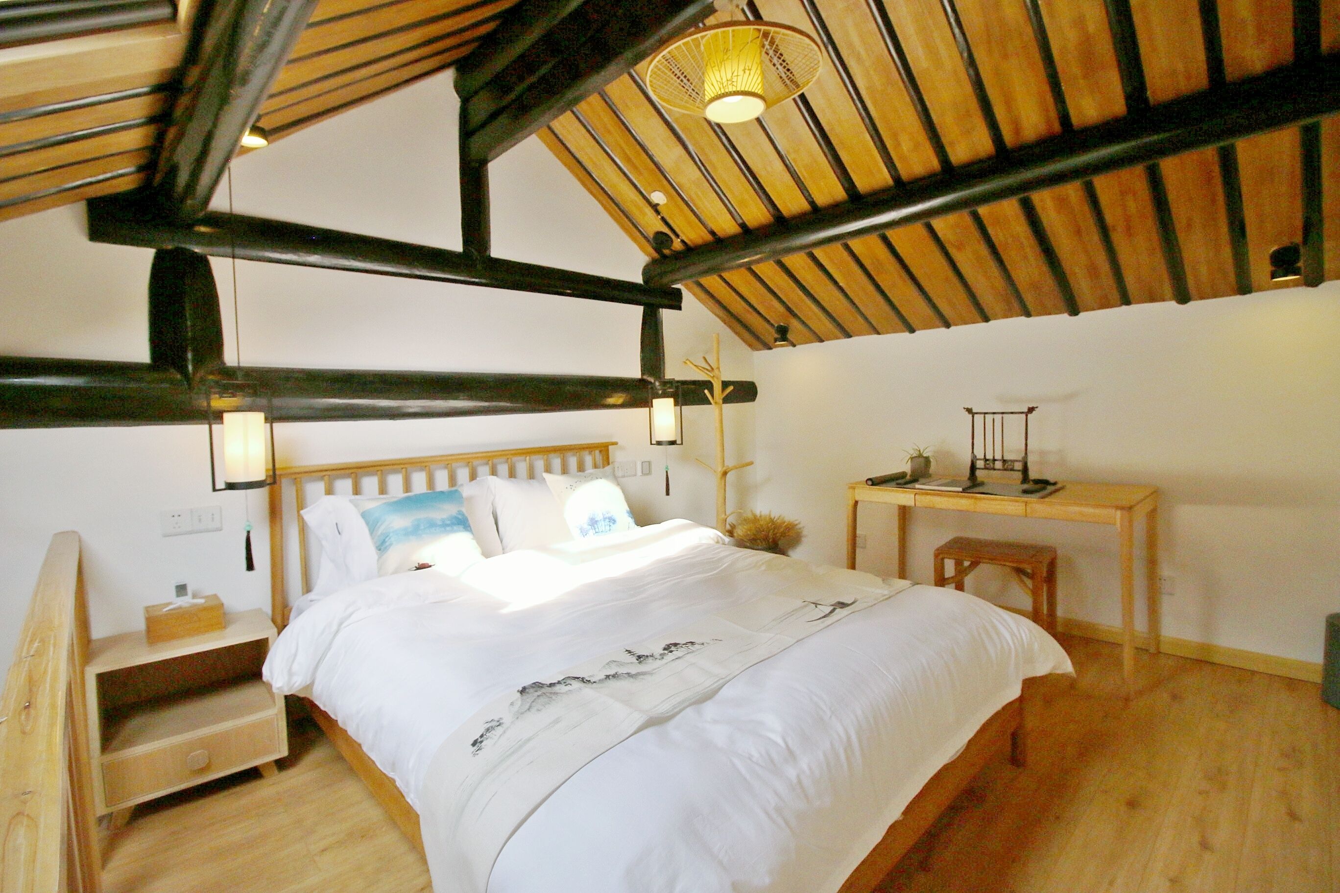 A bedroom with a wooden bed, a nightstand, a desk, and a hanging light fixture.