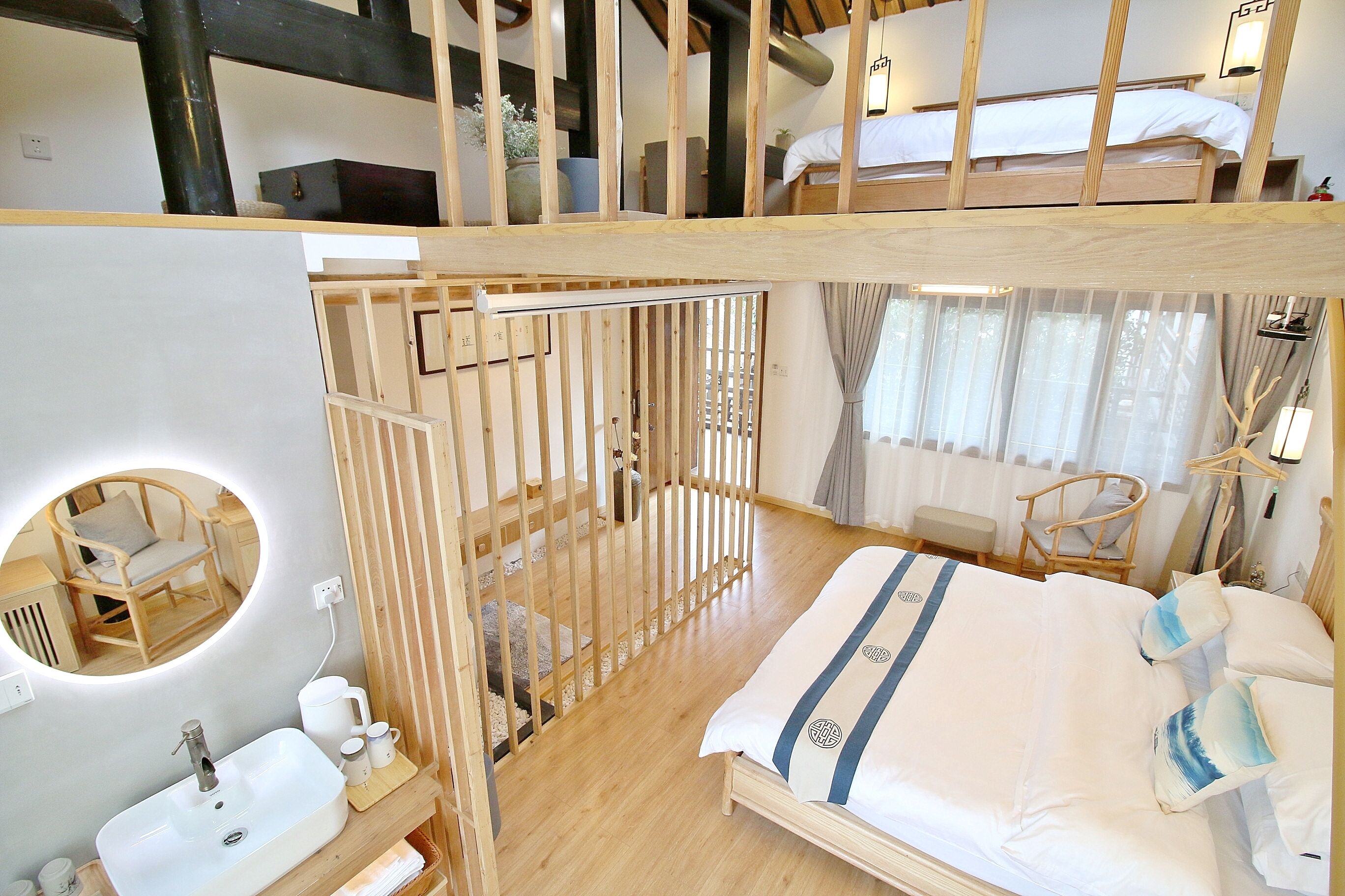 A room with a bunk bed, a round mirror, a wooden partition, a sink, and a bedside table.