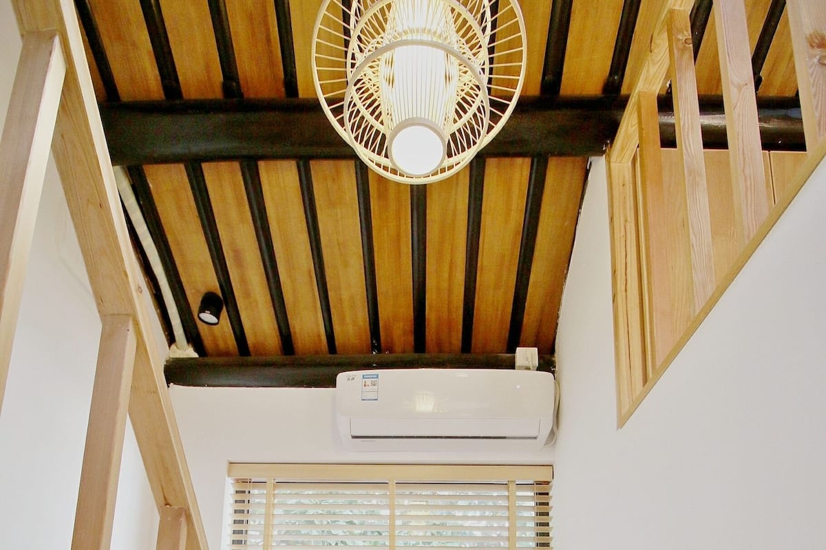 A staircase leading to a room with a wooden ceiling, a window with blinds, and an air conditioning unit.