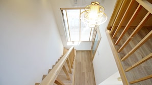 A wooden staircase with a modern light fixture, leading to a room with a wooden floor and a window with blinds. - shierpusu (Shaoxing)