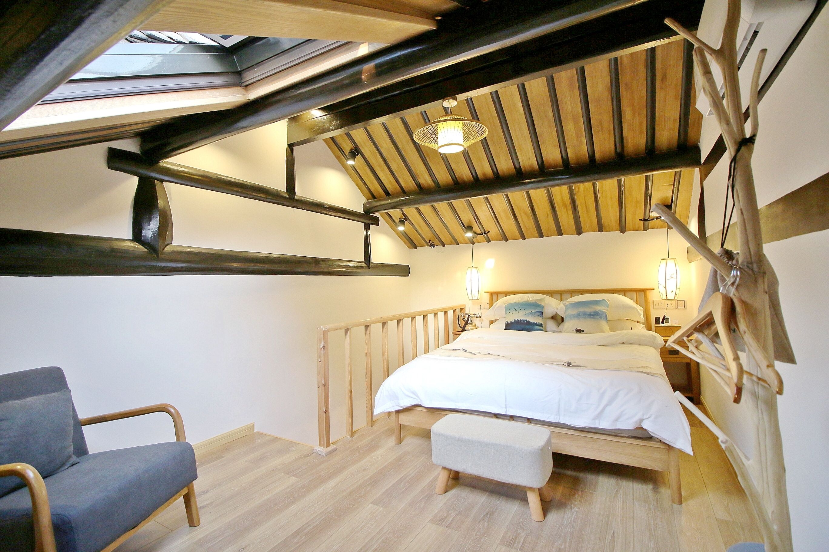 Um quarto com uma cama, uma cadeira, teto de madeira e um claraboia.