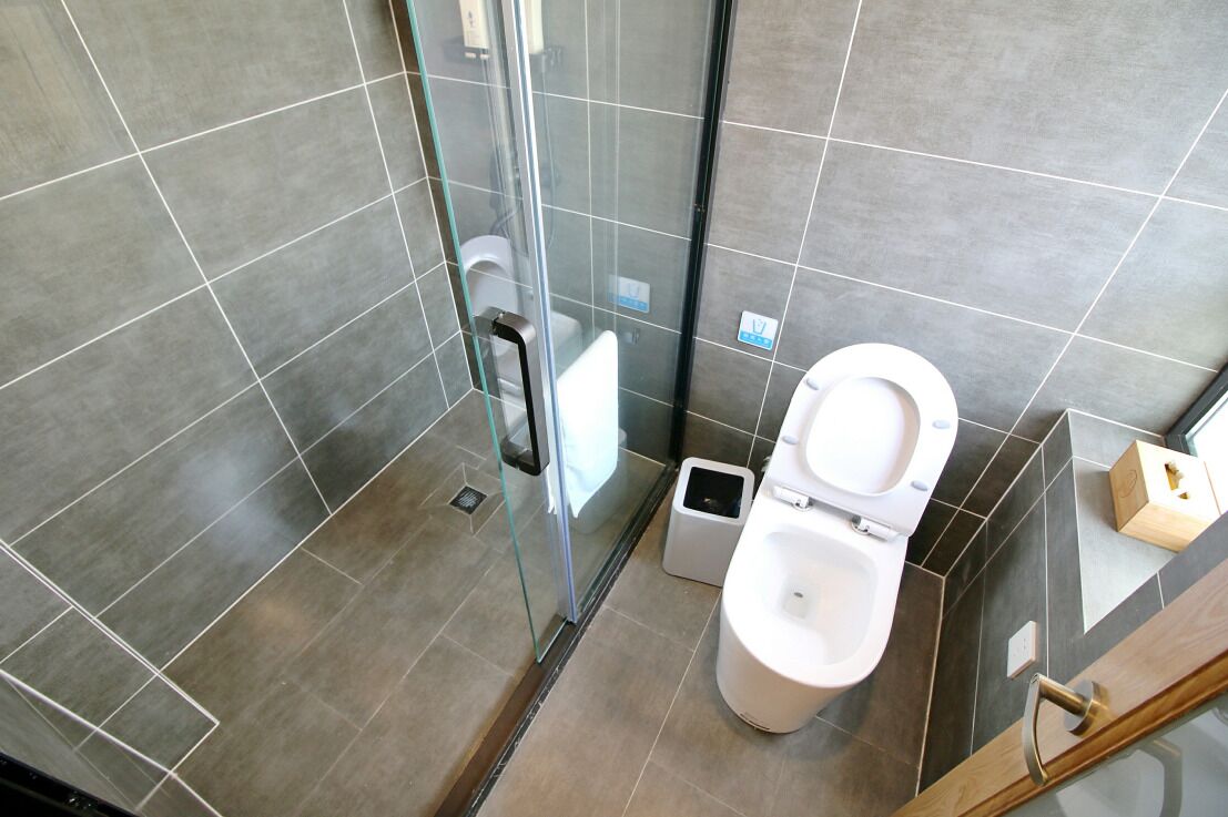 Un baño moderno con cabina de ducha de vidrio, inodoro blanco y un pequeño cubo de basura.