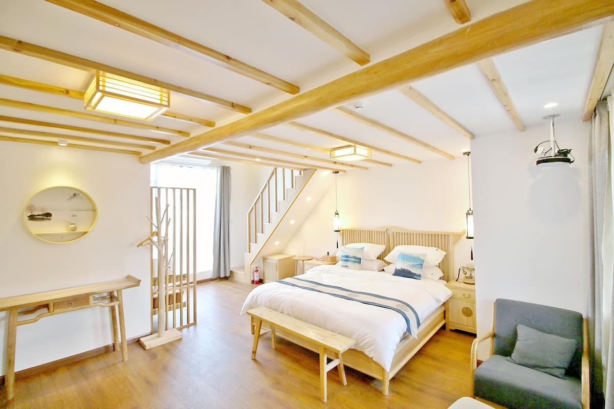 A bedroom with a bed, bench, chair, bedside table, and a staircase.