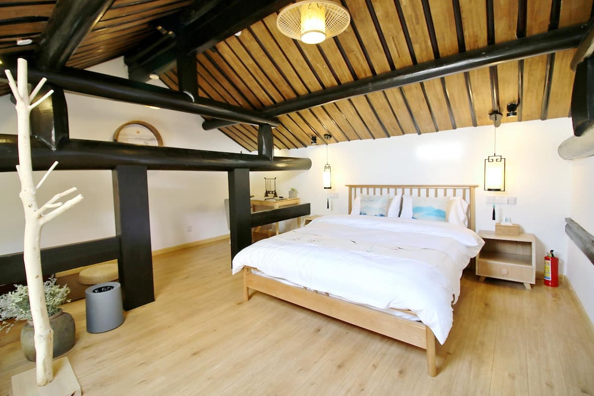 A bedroom with a wooden bed, a nightstand, a wall-mounted lamp, a hanging light fixture, and a small potted plant.