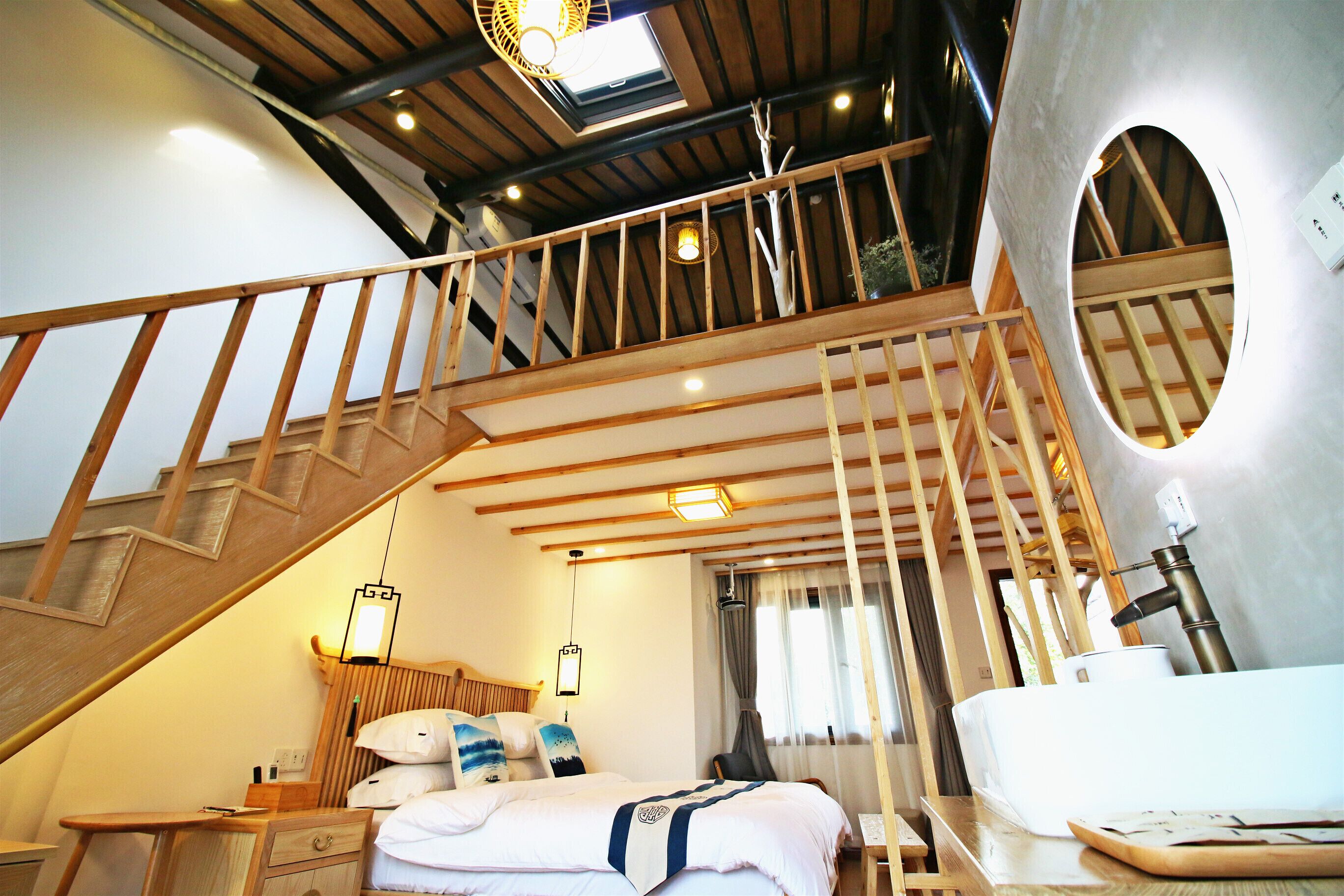 Une chambre d’hôtel avec un escalier en bois, un lit avec une literie blanche, une table de chevet et une salle de bain équipée d’un lavabo et d’un miroir.