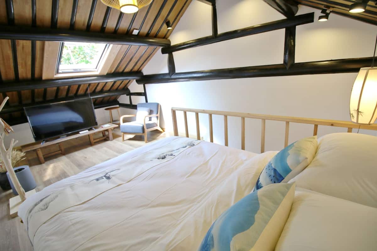 A bedroom with a bed, a TV, a chair, and a window.