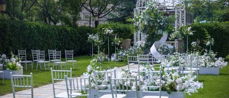 An outdoor wedding venue with white chairs arranged in rows, a gazebo, and lush greenery.
