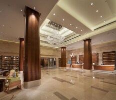 A spacious lobby with high ceilings, large wooden columns, a central chandelier, and a reception desk.