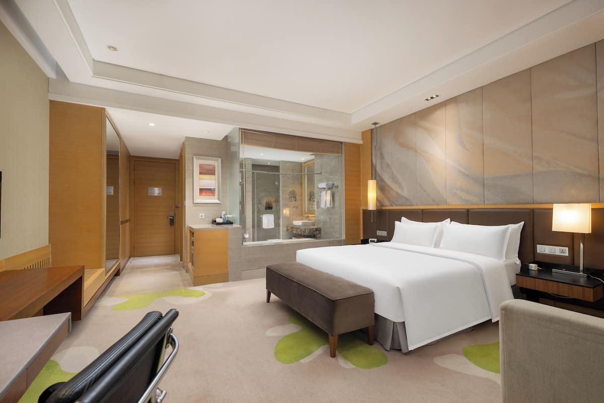 Ein Hotelzimmer mit Bett, einer Sitzbank, einem Schreibtisch, einem Stuhl, einem Spiegel und einem Badezimmer mit Dusche und Waschbecken.