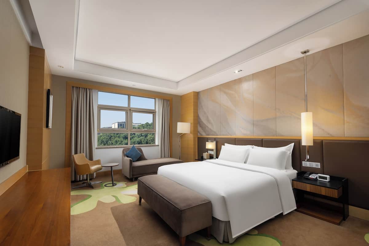 Ein Hotelzimmer mit Bett, Schreibtisch, Stuhl, Fernseher, Fenster und Lampe.
