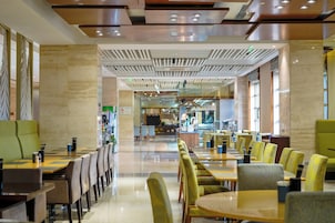 A spacious dining area with multiple tables and chairs, a central bar, and a modern ceiling design.