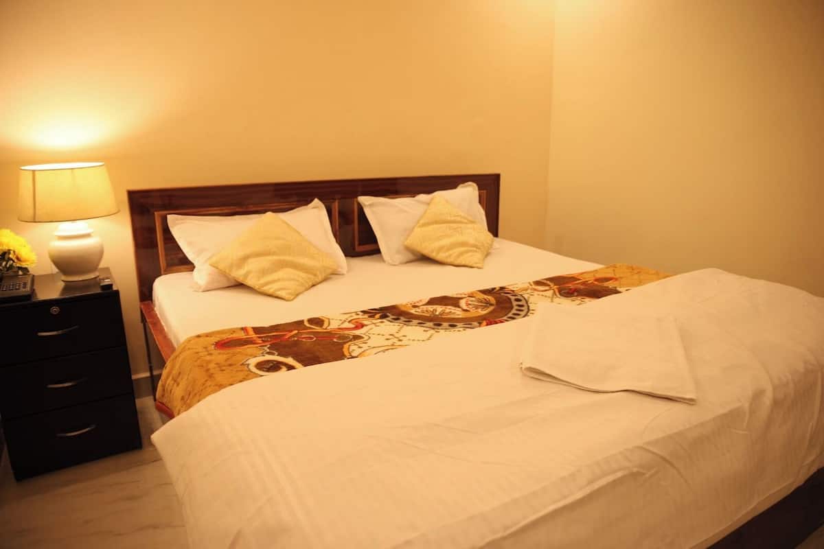 A neatly made bed with a patterned bedspread, two pillows, and a bedside lamp on a nightstand.