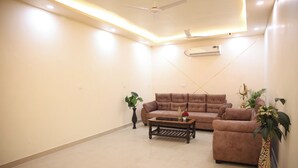 A spacious living room with a large brown sofa, a wooden coffee table, and two potted plants. - Hotel Kalpana (Patna)
