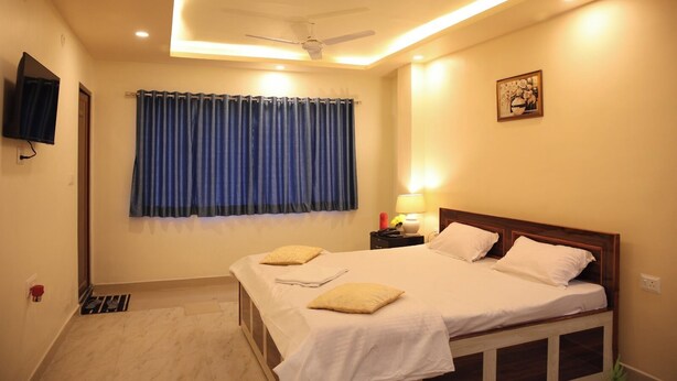 A hotel room with a bed, a ceiling fan, a nightstand with a lamp, and a television mounted on the wall. - Hotel Kalpana (Patna)