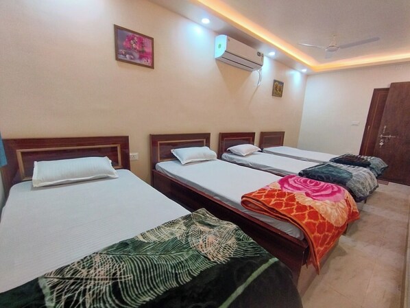 A hotel room with four single beds, an air conditioning unit, a ceiling fan, and a door. - Hotel Kalpana (Patna)
