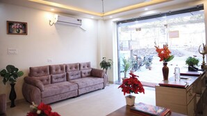 A modern living room with a sofa, a desk, and a large window. - Hotel Kalpana (Patna)
