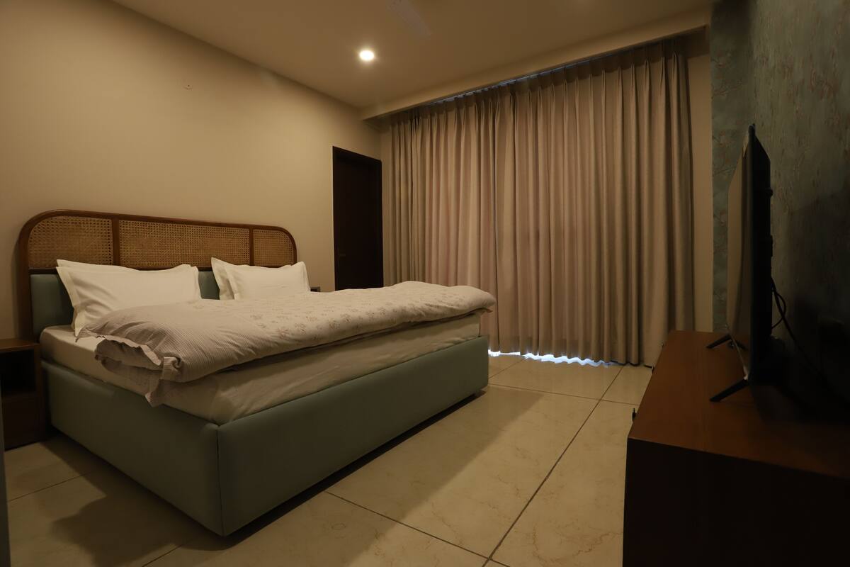 Ein modernes Hotelzimmer mit einem großen Bett, einem Flachbildfernseher und einem großen Fenster mit Vorhängen.