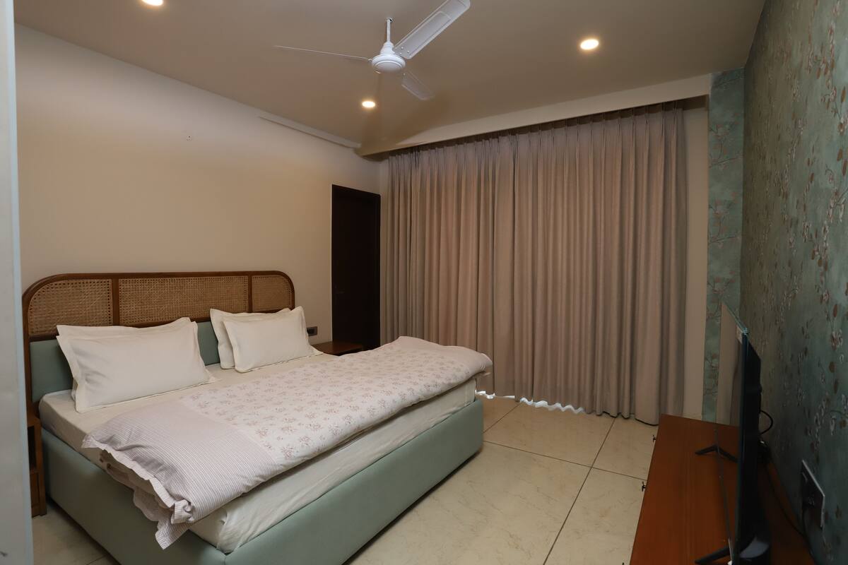 Ein Schlafzimmer mit Bett, Deckenventilator, Fernseher und Vorhang.