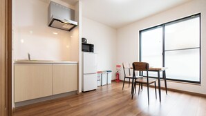 A modern kitchen with a microwave, refrigerator, and a dining area with a table and chairs. - HANASTAY KAWA (Osaka)