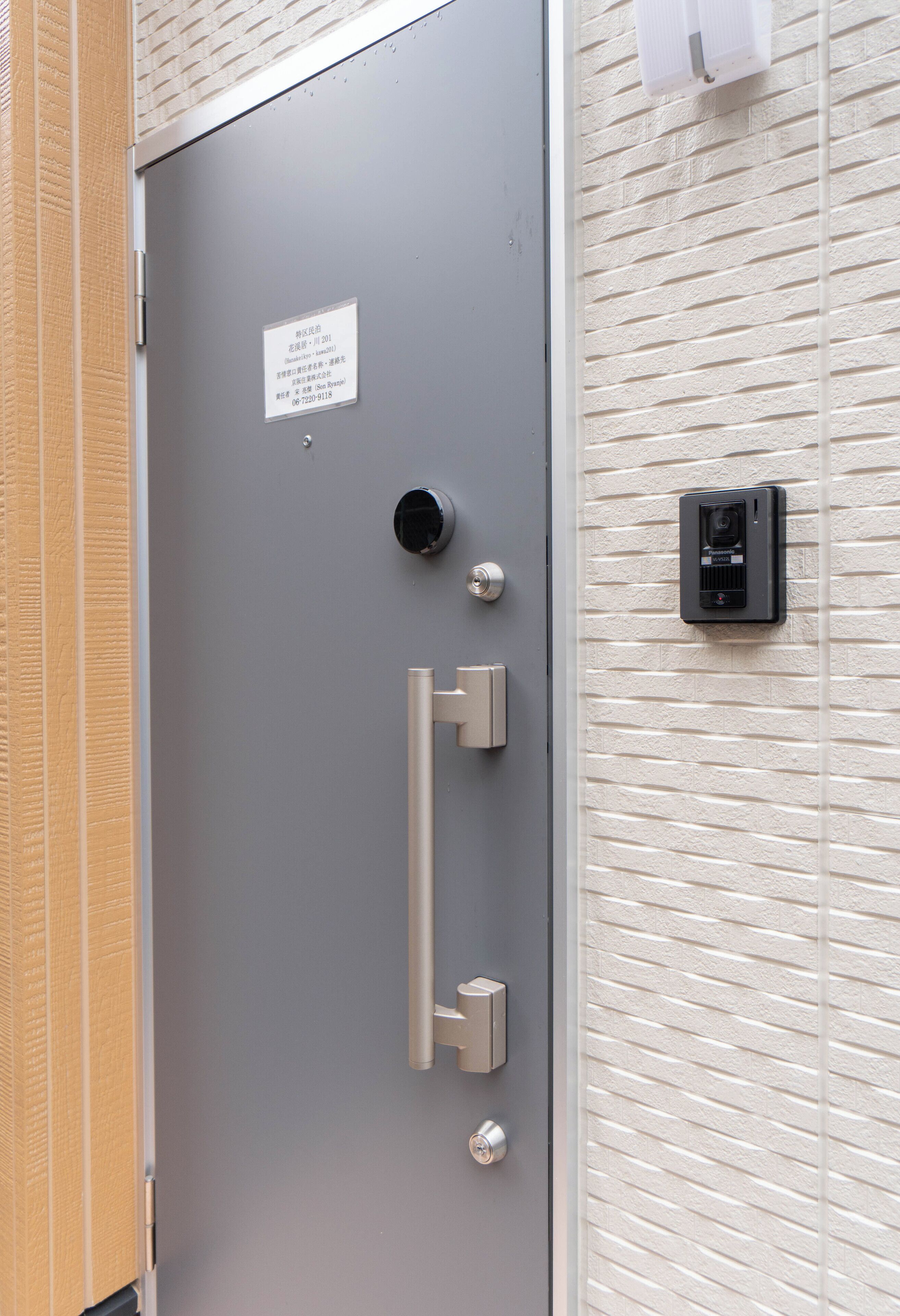 A gray door with a metal handle and a keyhole, a peephole, and a security camera mounted on the wall.