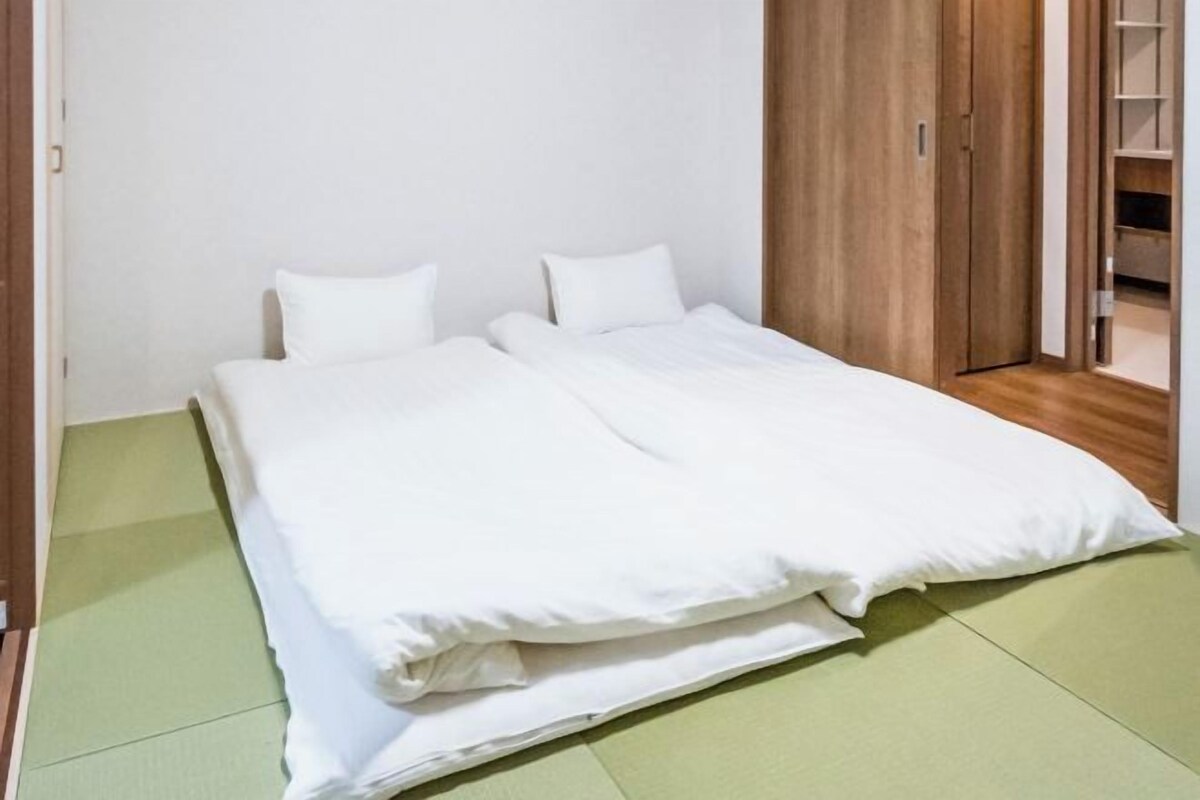 A single bed with white bedding in a room with a wooden wardrobe and a green mat on the floor.