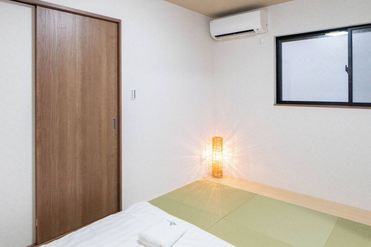 A hotel room with a bed, a wooden wardrobe, an air conditioning unit, a window, and a bedside lamp.
