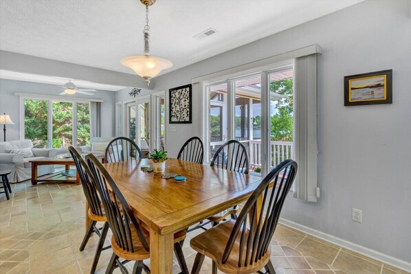 A spacious dining area with a wooden table and chairs, large windows, and a view of the outdoors.