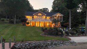 Une grande maison avec une pelouse bien entretenue et une jetée qui s’avance sur une étendue d’eau calme.