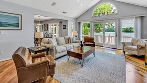Un salon spacieux avec un plafond haut, un ventilateur de plafond et de grandes fenêtres offrant une vue sur l’extérieur.