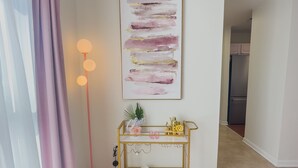 Ein modernes Wohnzimmer mit einem goldenen Konsolentisch, einer pinkfarbenen Stehlampe und einem großen abstrakten Gemälde an der Wand.