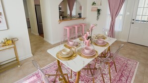 Ein Essbereich mit einem weißen Tisch, gedeckt für vier Personen, rosafarbenen Stühlen und einer goldenen Chandelier.