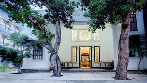 Un patio con la entrada de un edificio, árboles y un banco.
