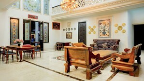 Un vestíbulo espacioso con techo alto, un candelabro, una zona de estar con sofá y sillones, y un comedor con mesa y sillas.