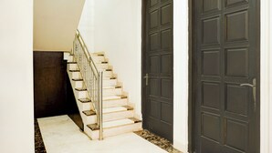 Una escalera conduce a una puerta oscura, con una pared blanca y un suelo oscuro.