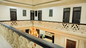 Una imponente escalera con barandales ornamentales y un candelabro, que conduce a un espacio con chimenea y área de cocina.