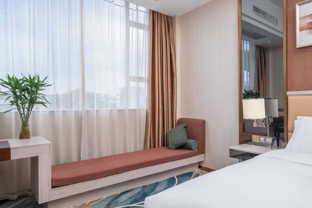 Een hotelkamer met een bed, een zithoek met een bank, een nachtkastje, een lamp en een plant.
