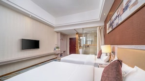 Quarto de hotel com duas camas, uma televisão de tela plana, banheiro com chuveiro de vidro e um quadro na parede.