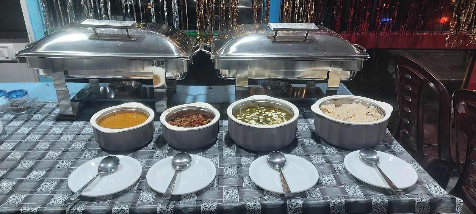 Una mesa de buffet con cinco fuentes de comida y cuatro platos con cucharas.