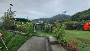 A pathway leading to a rustic building with a stone wall and a red flower decoration. - Nisarg Camping Pods (Almora)