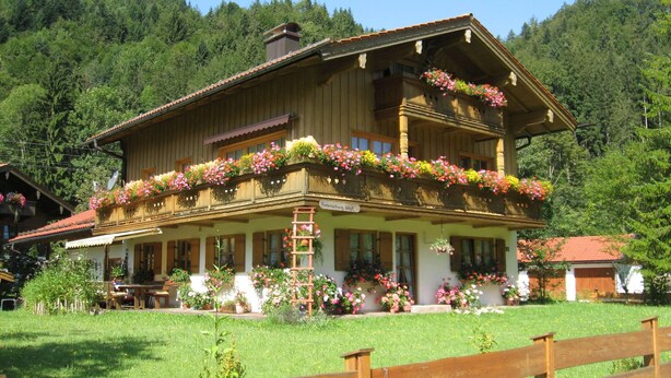 A traditional wooden house with a balcony adorned with flowers, surrounded by lush greenery and a wooden fence. - B Apartment Hörndl 52sqm, balcony, kitchen, 1 bedroom, 1 bedsit. (Ruhpolding)