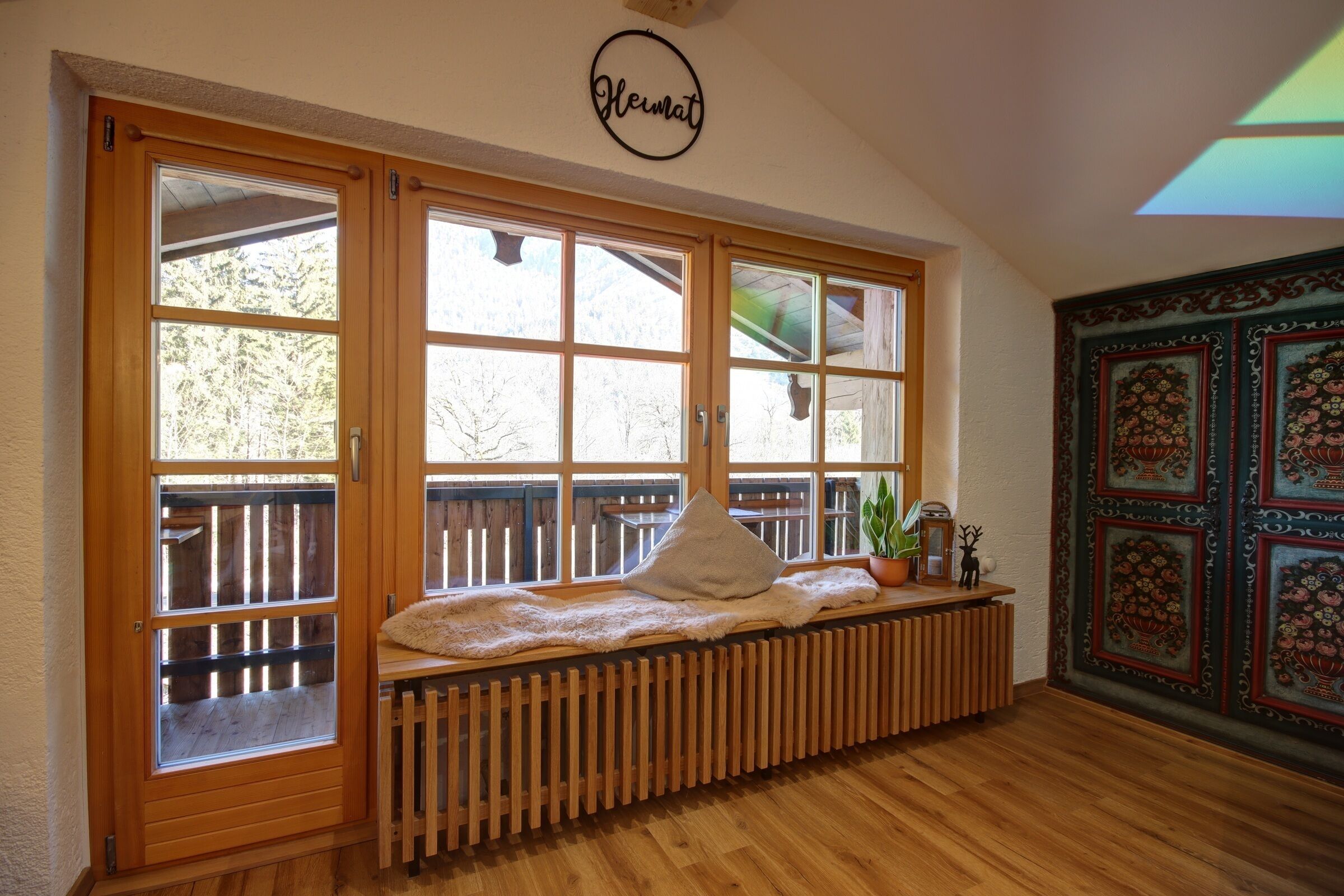 A room with a wooden bench by a large window, a radiator below, and a decorative wall panel to the right.