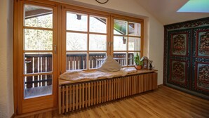 A room with a wooden bench by a large window, a radiator below, and a decorative wall panel to the right. - B Apartment Hörndl 52sqm, balcony, kitchen, 1 bedroom, 1 bedsit. (Ruhpolding)