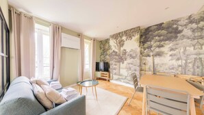 A living room with a sofa, a small round table, a dining table with chairs, and a TV.